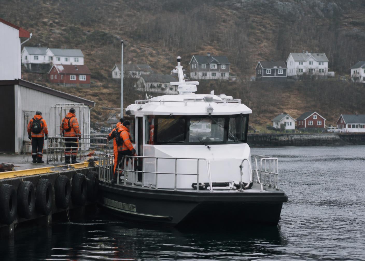 Arbeidsbåt ved kai der personell i oransje arbeidstøy går om bord